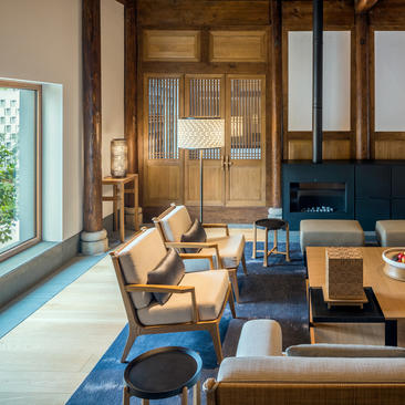 Amanyangyun lounge with wooden screens, natural light from windows, and contemporary furnishings on blue flooring.