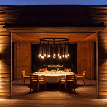 Three-bedroom residence dining pavilion at Amanoi, Vietnam, illuminated at night with round table and pendant lights.