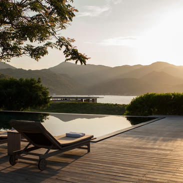 Wooden deck with lounge chair overlooking a calm bay at Amanoi, Vietnam, at dusk.