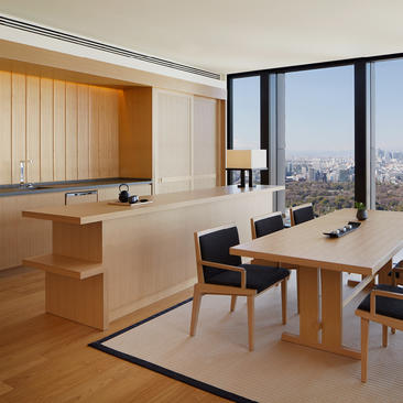 Aman Tokyo suite with open-plan living space, wooden kitchen, dining table and Tokyo skyline views through floor-to-ceiling windows.