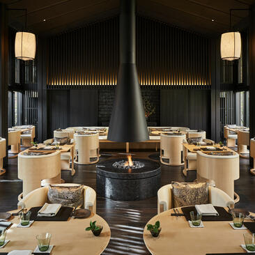 アマン京都のダイニング会場、中央に黒い暖炉を備えた対称的なテーブル配置。