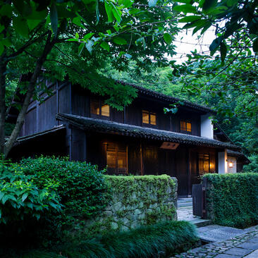 Traditional wooden residence surrounded by lush greenery at Amanfayun, illuminated at dusk.
