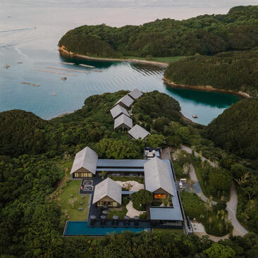 Aerial view of Amanemu resort nestled along a Japanese coastline, with white buildings surrounded by forested hills and blue waters.
