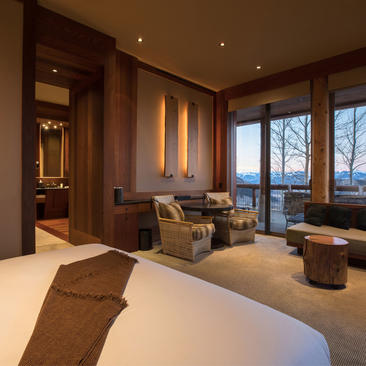 Shoshone Suite bedroom at Amangani with dual beds, warm wood panelling, and mountain views through floor-to-ceiling windows.