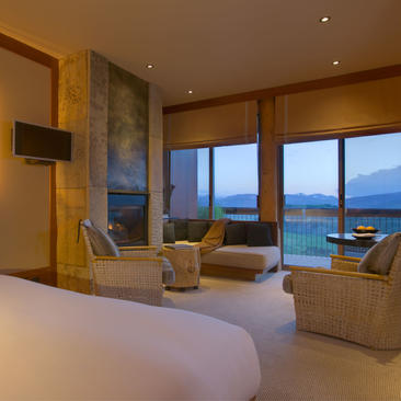 Superior Suite at Amangani with bed, seating area, and expansive windows overlooking mountain landscape at dusk.
