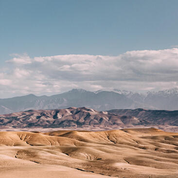 Amanjena's surrounding desert landscape with rolling sand dunes and distant mountain peaks beneath a clear sky.