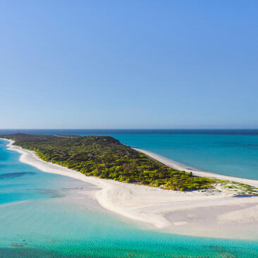 Aerial view of Amanpulo's sandy island peninsula with turquoise waters and dense vegetation.