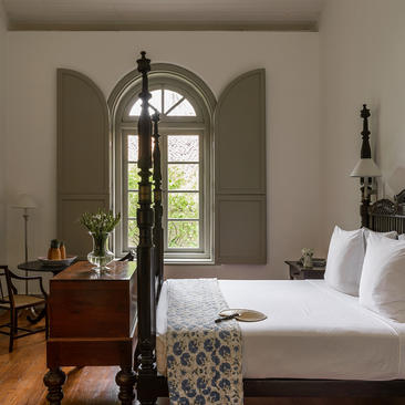 Principal bedroom at Amangalla with four-poster bed and arched window overlooking gardens.