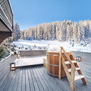 Wooden hot tub on a terrace at Aman Le Mélézin, overlooking snow-covered pine forests in the French Alps.