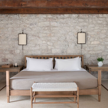 Principal bedroom at Aman Sveti Stefan with wooden bed, hanging lanterns, and neutral stone wall.