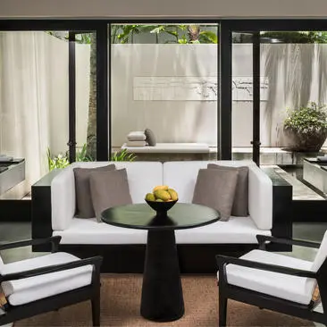Courtyard Suite sitting area at Amansara with curved seating, black round table, and garden views through floor-to-ceiling windows.
