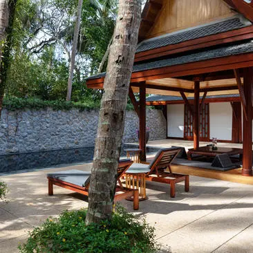 Garden pool pavilion at Amanpuri with wooden lounge chairs beneath a timber structure, framed by tropical trees.