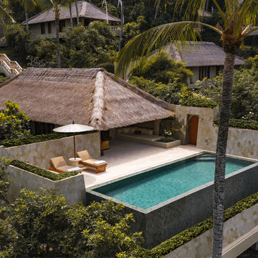 Infinity pool suite with thatched-roof pavilion at Amankila resort, Bali, surrounded by tropical gardens.