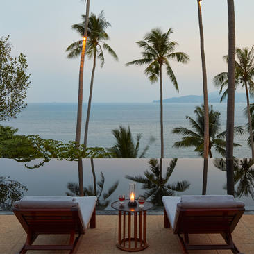 安缦璞瑞度假村的九卧室海景别墅，配有两张棕色躺椅和海景观台，背景是棕榈树和蔚蓝的安达曼海。