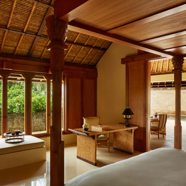 Amankila resort pool suite with warm wooden beams, natural light, and serene furnishings overlooking gardens.