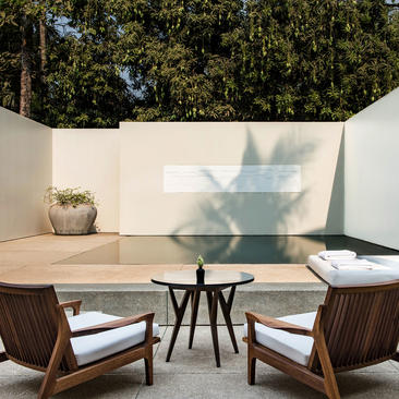 Pool Suite seating area at Amansara, with chairs facing a plunge pool and white walls casting dappled shadows.