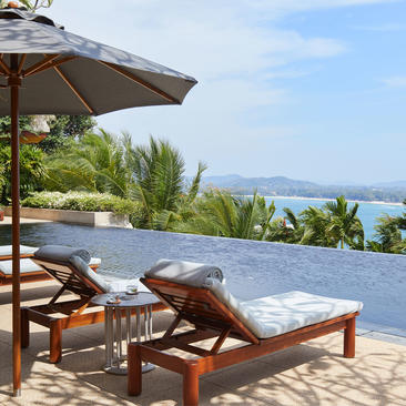 两张木制躺椅靠近游泳池边，背靠遮阳伞，俯瞰安缦璞瑞度假村的海景。