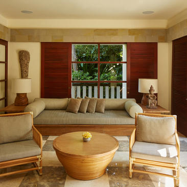 Six-bedroom villa living area with wooden furnishings and garden views at Aman Villas at Nusa Dua, Bali.