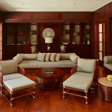 Principal bedroom at Aman Villas at Nusa Dua with warm wood panelling, cream armchairs and a draped bed.