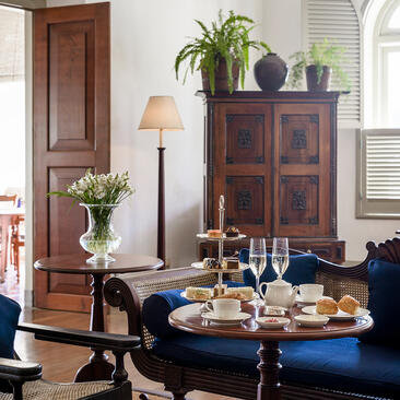 Afternoon tea service laid out on a dark wooden table at Amangalla, with a navy sofa and traditional wooden furniture in the background.