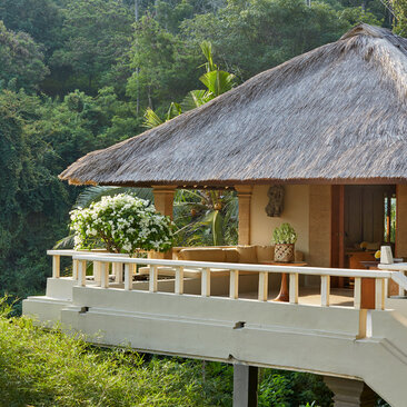 Amankila resort pavilion with thatched roof nestled amongst lush tropical vegetation and verdant hillside.