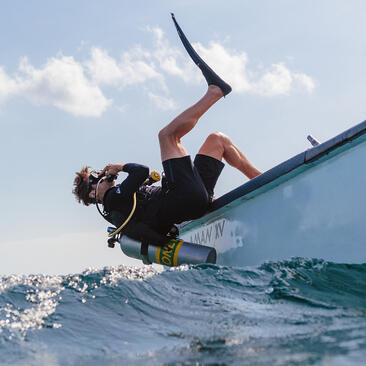 Person wakeboarding behind a boat at Amanwana, suspended mid-air above sparkling water.