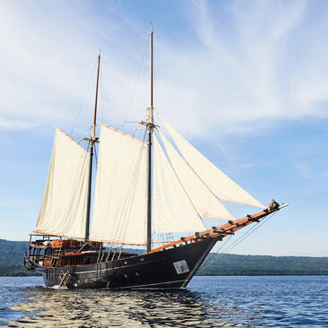 Traditional sailing vessel with cream canvas sails on blue water at Amandira, Indonesia.