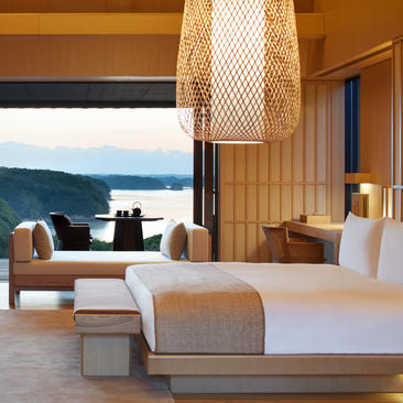 Nagi Suite bedroom with panoramic bay views at Amanemu resort, featuring a bed, seating area and floor-to-ceiling windows.