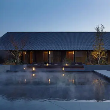 Amanemu resort's outdoor spa at dusk, with a modern pavilion reflected in still water beneath a clear sky.