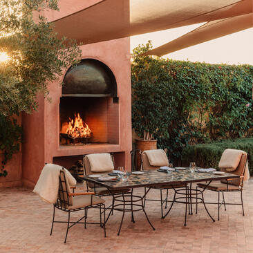 Terracotta courtyard dining area at Amanjena with table, chairs, and fireplace alcove.