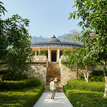 Stone walkway lined with tropical foliage leading towards a pavilion at Amanjiwo, Java.