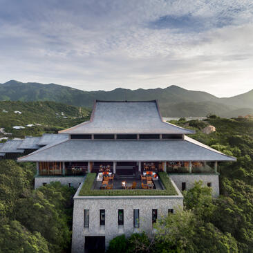 Amanoi's architectural pavilion with sweeping roof overlooks forested valley and distant mountains.