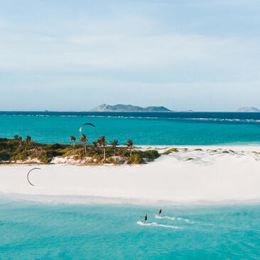 Aerial view of a white sand beach and turquoise waters at Amanpulo, with a distant island on the horizon.