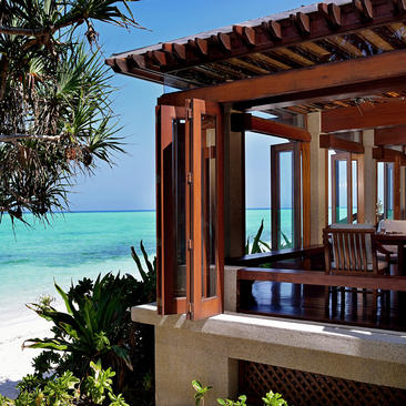 Wooden pavilion at Amanpulo with turquoise sea views, featuring open shutters and tropical plants.