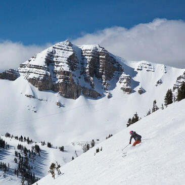 Snowy mountain landscape at Amangani with skiers descending a white slope beneath a dramatic rocky peak.