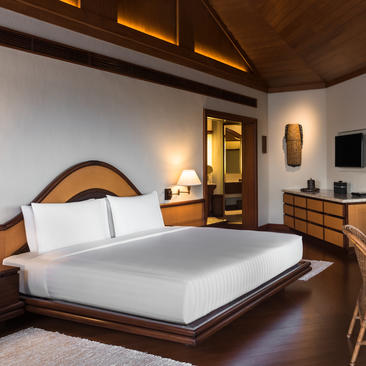 Chambre avec lit king-size en bois sombre, draps blancs et lampes murales dorées à Amanpulo, resort aux Philippines.