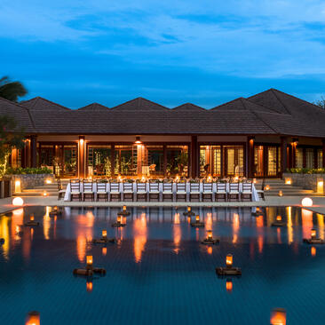 West Villa Clubhouse at Amanpulo illuminated at dusk, reflected in still water beneath twilight sky.