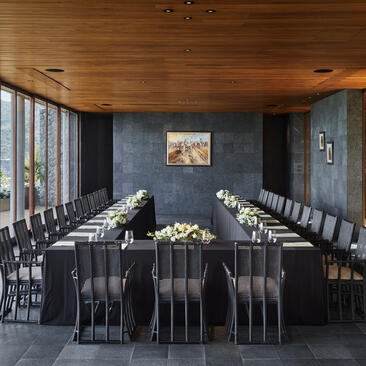 Dining pavilion at Amanpuri with long dark table, black chairs and floor-to-ceiling windows overlooking the landscape.