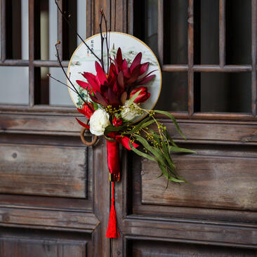 Floral arrangement with red and white flowers tied with ribbon on wooden door at Amanfayun.