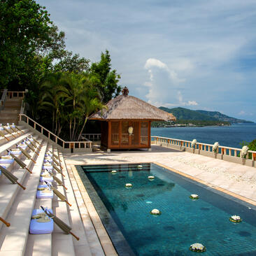 Amankila's clifftop plunge pool overlooks the Lombok Strait, with sun loungers and wooden deck in foreground.