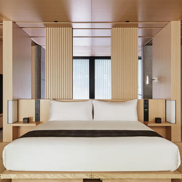 アマン京都のリゾートの寝室。白いベッドと木製のフレームが、天井窓から自然光が差し込む広々とした空間に配置されている。