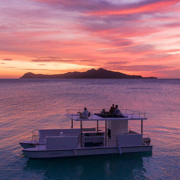 Floating pontoon at sunset with pink and purple skies, Amanpulo resort.