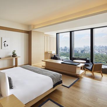 Deluxe bedroom at Aman Tokyo with wooden flooring, floor-to-ceiling windows overlooking the city, and minimalist furnishings.