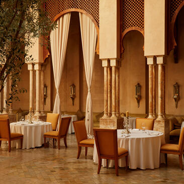 Amanjena dining venue with arched doorways, warm terracotta tones, and intimate table settings beneath Moroccan architecture.