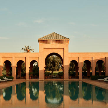 Amanjena's pavilion with arched colonnade reflected in still courtyard pool at sunset.