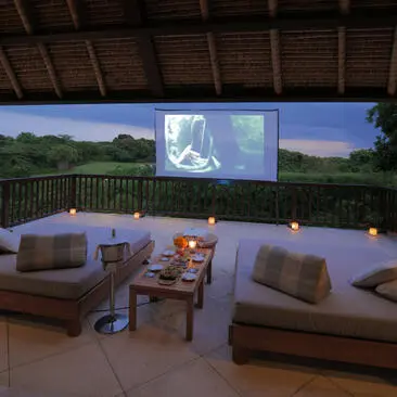 Outdoor pavilion at Aman Villas at Nusa Dua with seating and projection screen showing film during evening.
