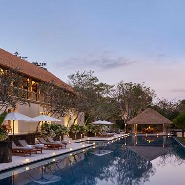 Aman Villas at Nusa Dua villa with illuminated interior, viewing pool and manicured gardens at dusk.