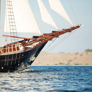 Traditional wooden sailing vessel with billowed sails off the coast of Amandira, Indonesia.