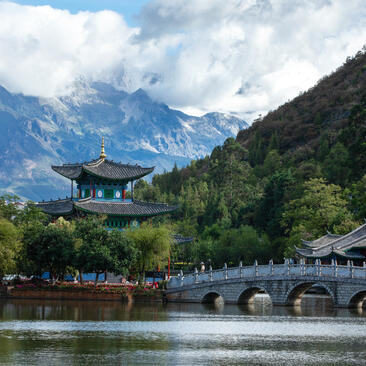 大研安缦度假村的黑龙潭景观，远处雪山环绕，石桥横跨平静水面。