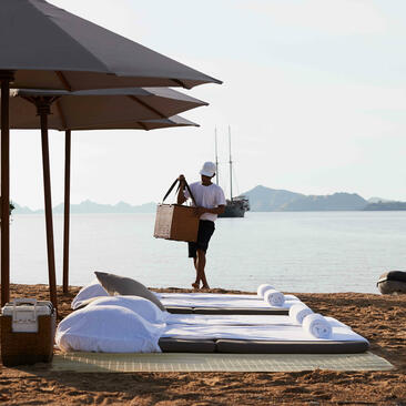 Woman sitting under a canopy at Amandira's beachside picnic setup, with kayak and sea views beyond.